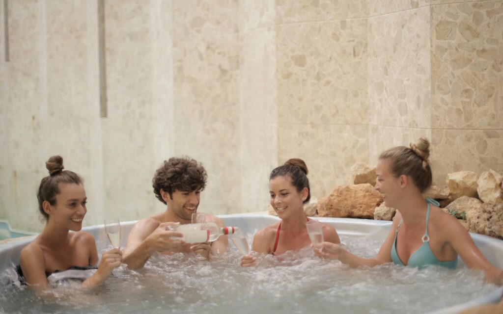 Friends having fun and relaxing together in a jacuzzi with drinks indoors.